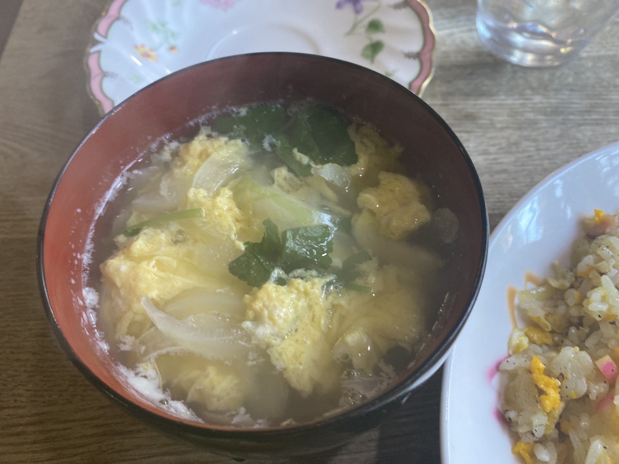 赤い漆椀に卵・白菜・青菜の入ったスープ、隣に炒飯の皿