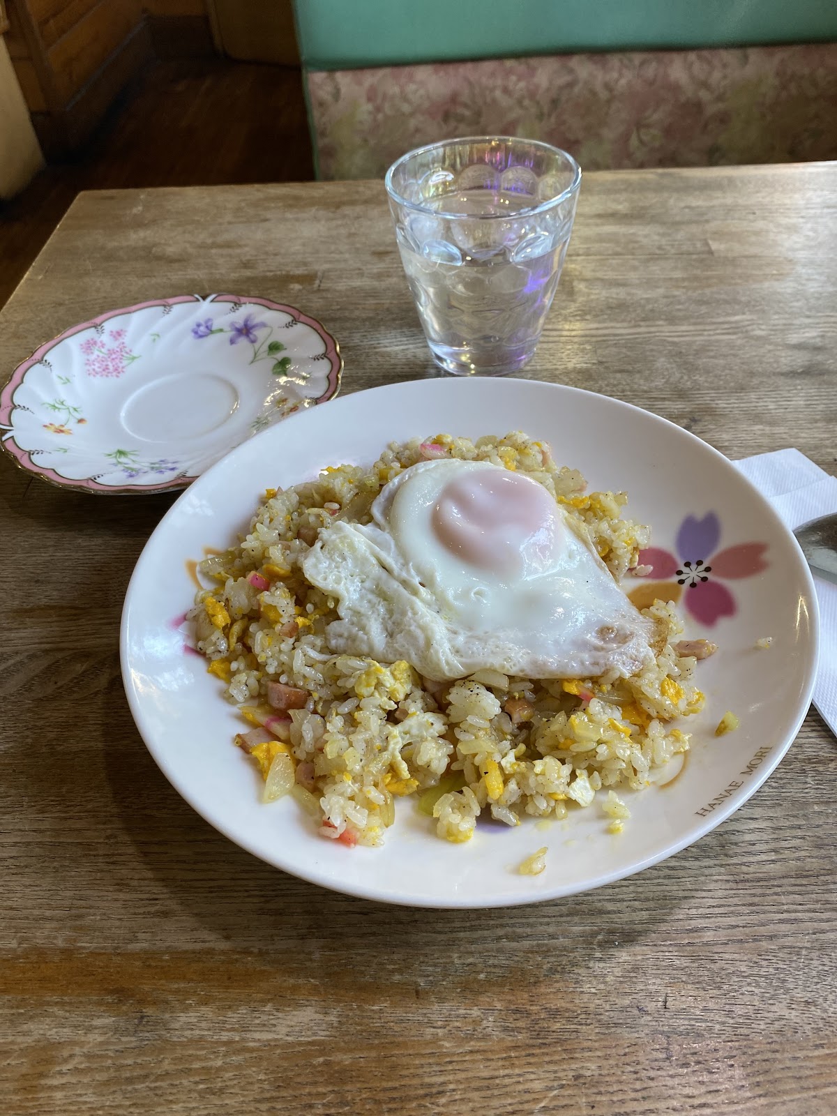 花柄皿の上に目玉焼きをのせた炒飯、背後に水の入ったガラスコップとソーサー